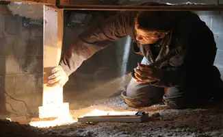A professional inspecting wooden beams under the floor of a structure in Dallas, TX