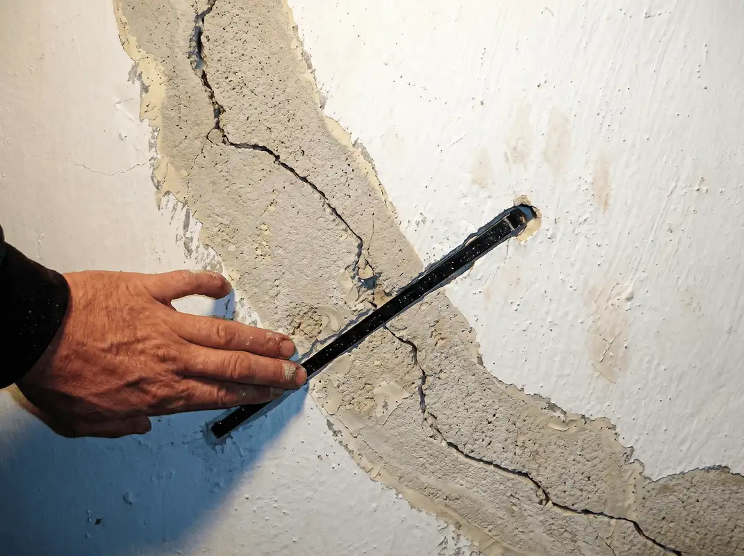 A wall with a large crack is being inspected by a professional in Dallas, TX