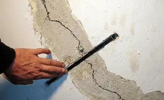 A wall with a large crack is being inspected by a professional in Dallas, TX